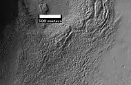Surface of Debris Apron. There is also a feature similar to features in Red Rocks Park Colorado.  Feature seems to be composed of slanted rock layers.  Image taken with HiRISE, under the HiWish program.