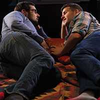 Photo of two men lying on a blanket, facing each other, talking.