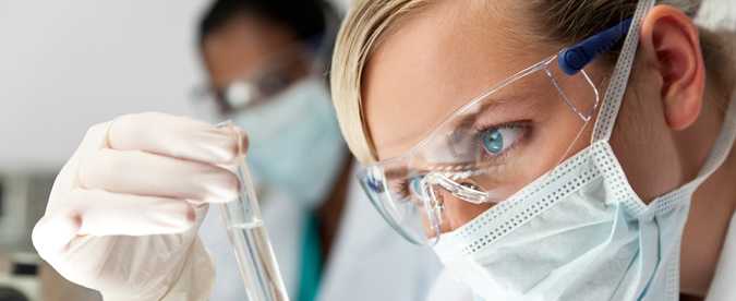 A laboratory worker examines a specimen in a tube.