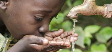 Young boy drinking from a faucet