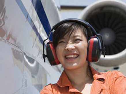 Woman wearing hearing protection while standing next to plane.